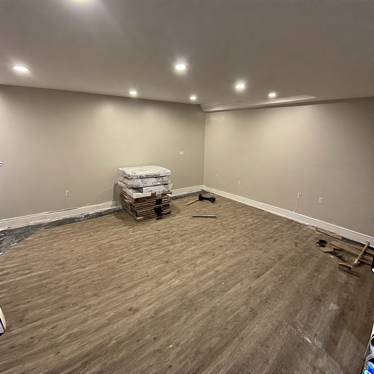 Basement Remodeling in Chicago 13 Basement room with newly installed moisture-resistant luxury vinyl plank flooring, stacks of flooring materials, and recessed lighting, showcasing a renovated space ready for functional living areas.